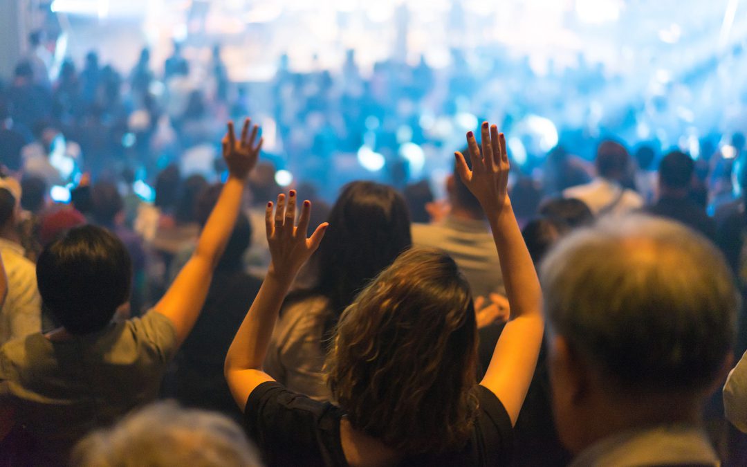 Audience members raising their hands at a lively indoor event.